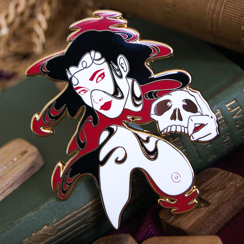 Enamel pin depicting a woman with long black hair in a pool of blood. She has one shoulder and breast above the liquid, and her opposite hand holds a skull.