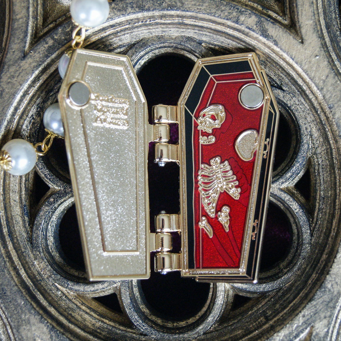 Photo of an enamel pin that is on a hinge, open to show a skeleton submerged in blood. 