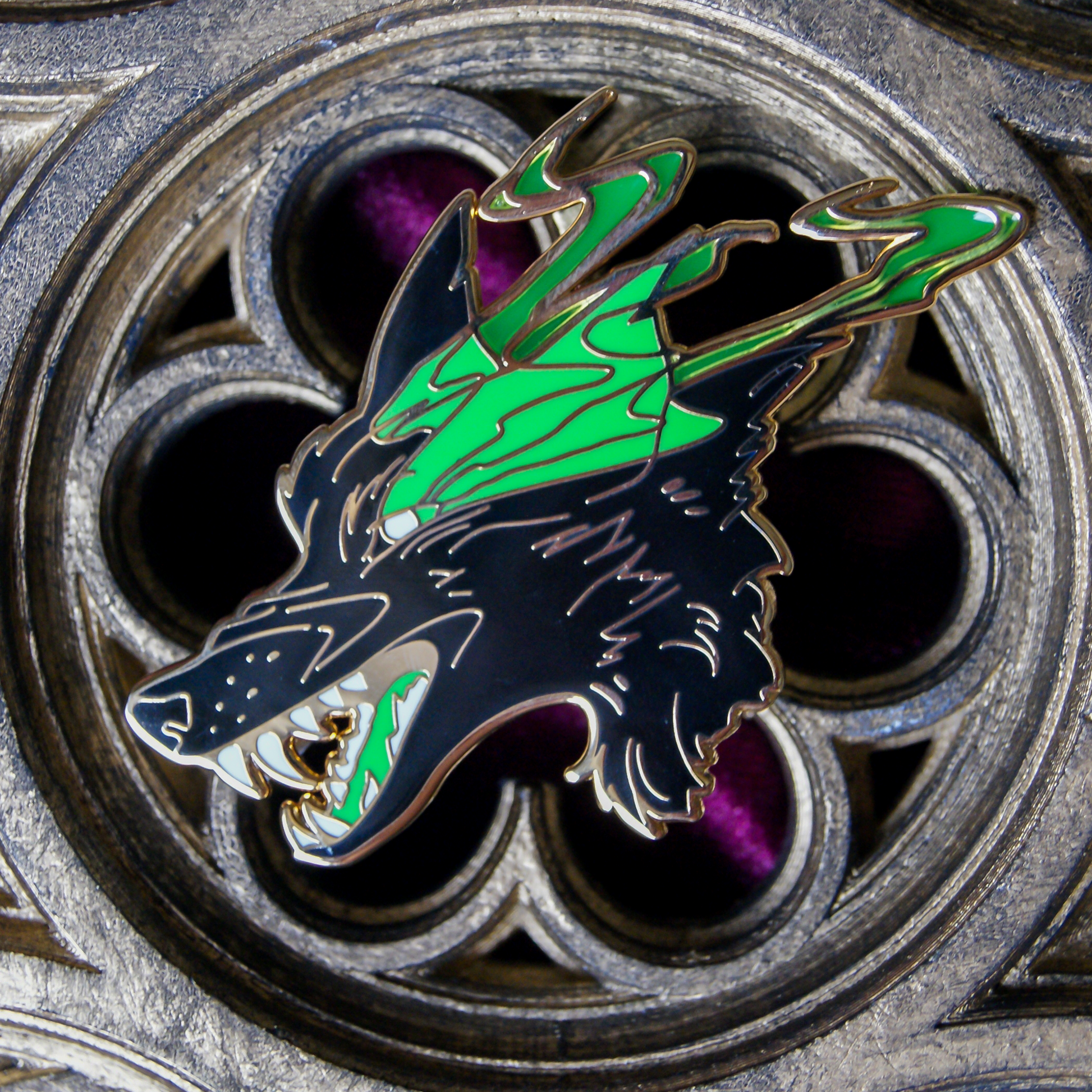 Enamel pin depicting a wolf in black with smoking, glowing green eyes. The background is a gothic church window carving.