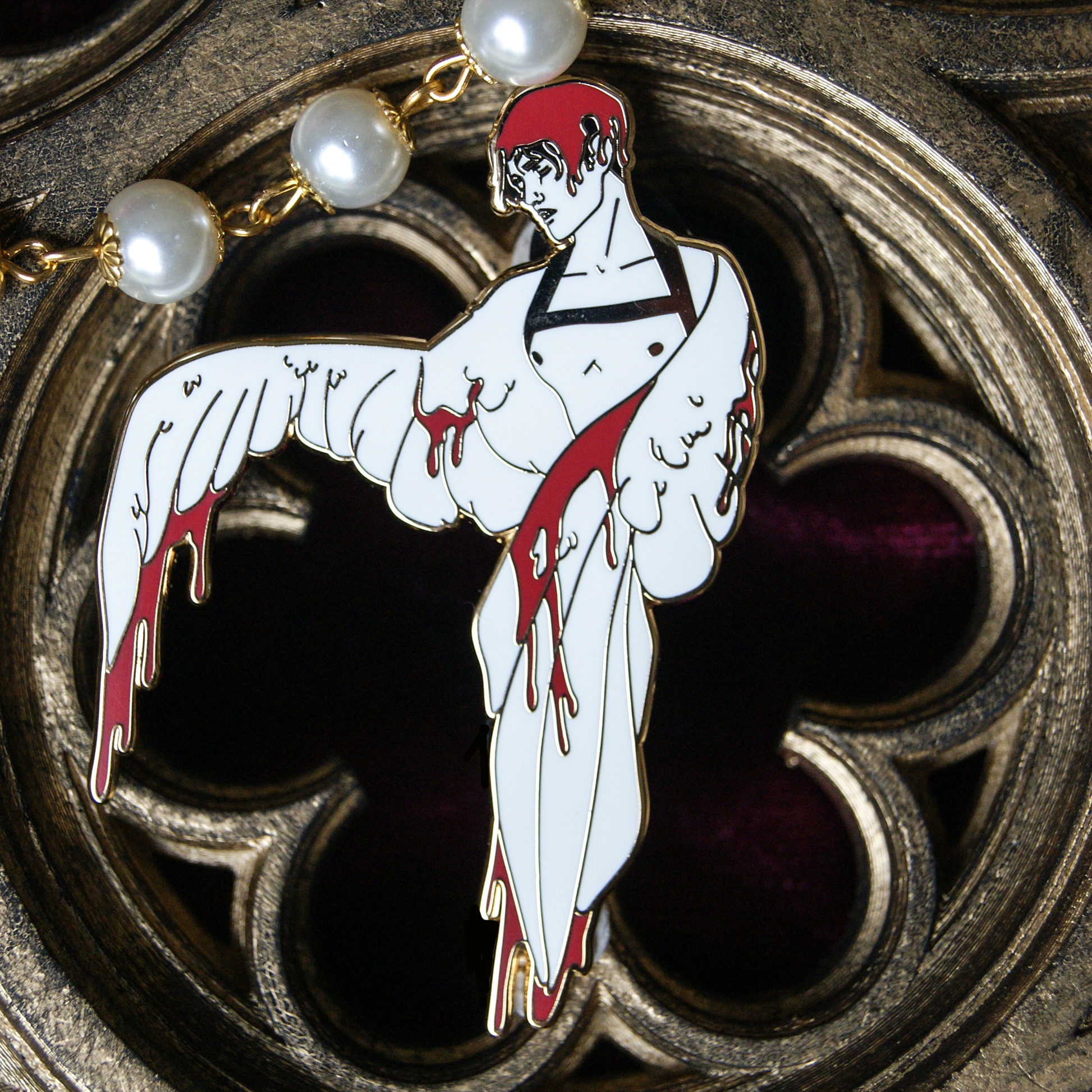 Photograph of an enamel pin depicting Icarus. He has two wings instead of arms, and wax in red drips from the feathers and also over his hair. Behind the pin is a gothic carving. 