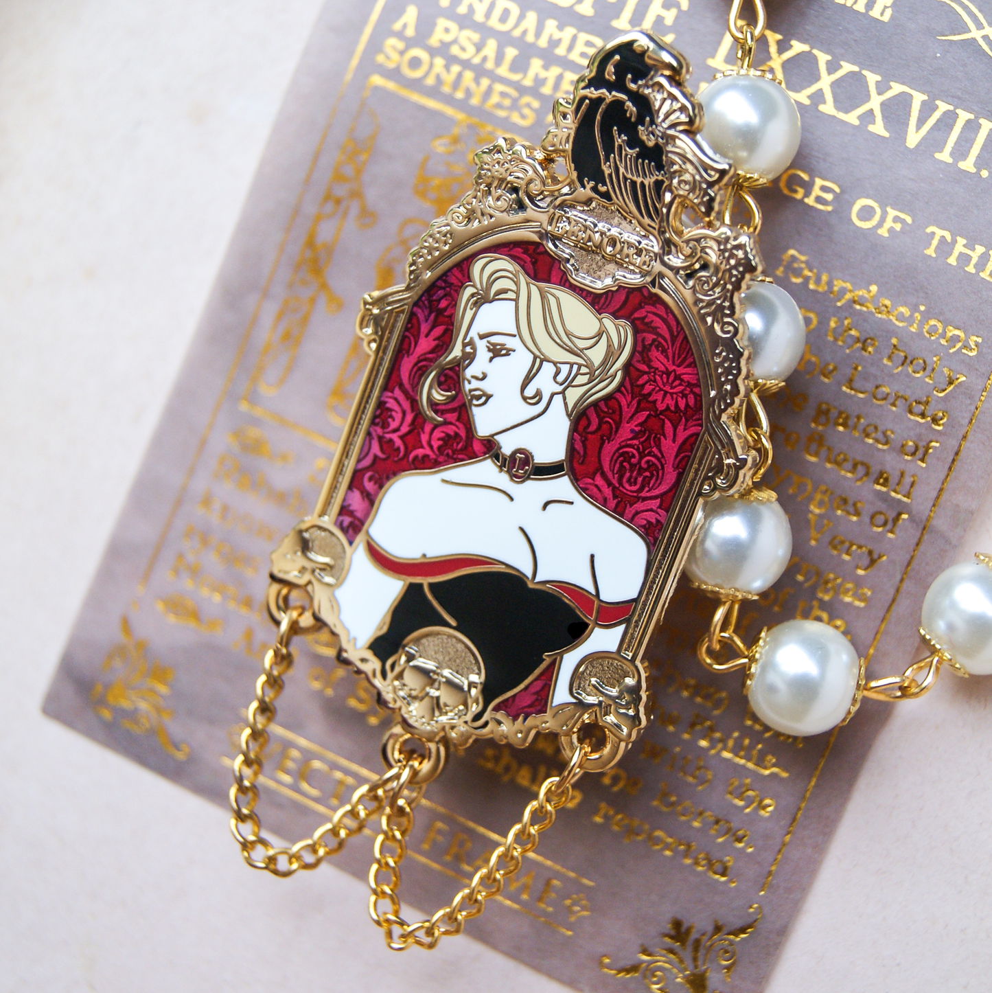 Enamel pin depicting a portrait of a woman with blonde hair and a low cut dress. Above her is a black raven and below her are golden skulls and chains. Behind the pin is a book page and pearls. 