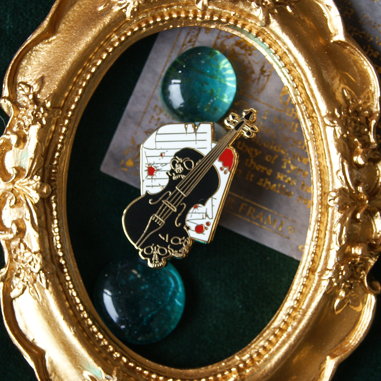 Enamel pin depicting a black violin on top of bloodstained music sheets. The violin has warped into skull shapes. The background is green jewels and a golden frame.