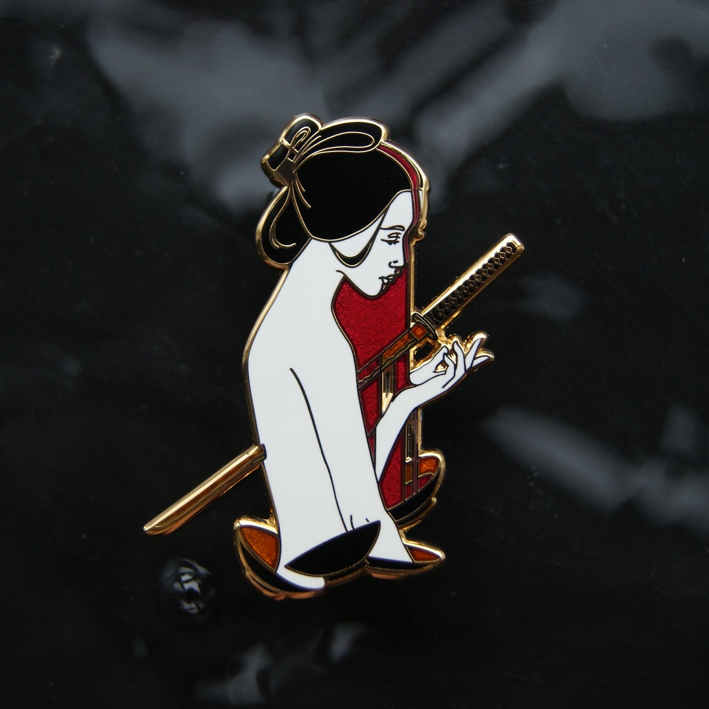 Enamel pin depicting the ghost Okiku - a Japanese woman with a sword through her and cups below her. The background is dark water.