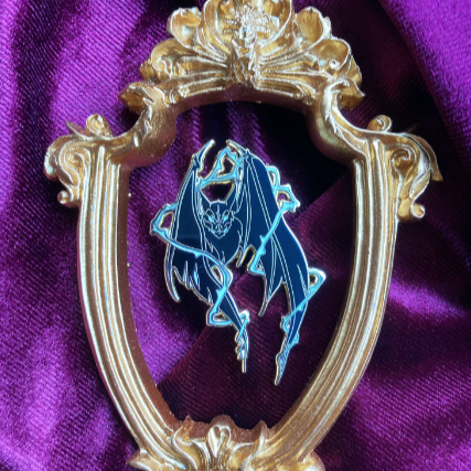 Photograph of an enamel pin depicting a bat surrounded by thorns. 